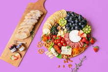 Load image into Gallery viewer, A colourful assortment of artisan cheeses, grapes, strawberries, kiwi, cherry tomatoes, dried apricots, turkey rolls, smoked salmon, nuts, crackers and sliced baguette arranged on a round wooden boards.