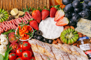 A colourful assortment of artisan cheeses, grapes, strawberries, kiwi, cherry tomatoes, dried apricots, turkey rolls, smoked salmon, nuts, and crackers that fills up the entire image.