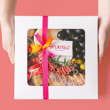 Load image into Gallery viewer, Splatter&#39;s Cheese &amp; Meat Platter in a covered white box with transparent window that shows most of its content. Pink and orange ribbons form a knot in the middle with a tag branded with Splatter&#39;s logo. Two hands hold the side of the box.