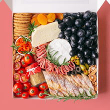 Load image into Gallery viewer, A white square box is packed to the brim with a soft cheese wheel and semi-firm cheese block accompanied by black grapes, cherry tomatoes, green olives, black olives, smoked salmon, turkey rolls, jar of wholegrain mustard, dried apricots, roasted almonds, walnuts, crackers, and baguette slices.